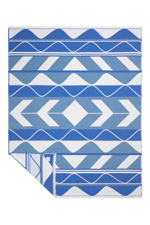 A beautiful blue and white Indigenous blanket shown flat against a white background with one corner folded over to reveal the reverse side.