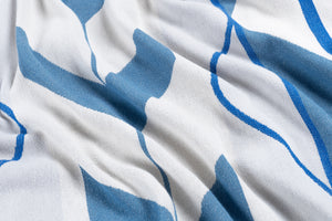 A close-up of a white and blue woven Indigenous blanket showing the soft texture and folds of the material.