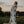 A woman stands outdoors in a grassy field at dusk, wrapped in a large white Indigenous blanket. 