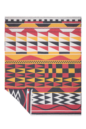 A folded blanket with a vibrant  pattern in red, yellow, black, and white, displayed on a clean white background.
