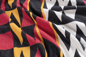 A close-up of a woven textile with a bold pattern in black, white, red, and mustard yellow, draped to show its texture and colors. 
