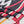A close-up of a woven textile with fringe, featuring a bold pattern in charcoal gray, red, white, and mustard yellow. 