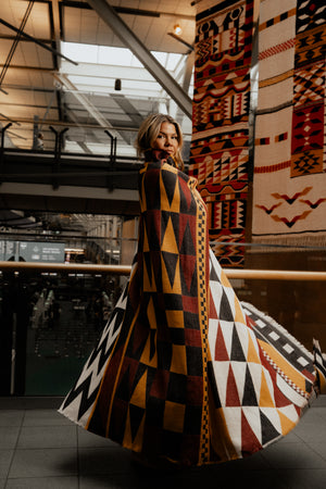 A woman wrapped in a blanket spinning indoors with large similar blankets hanging from the ceiling. 